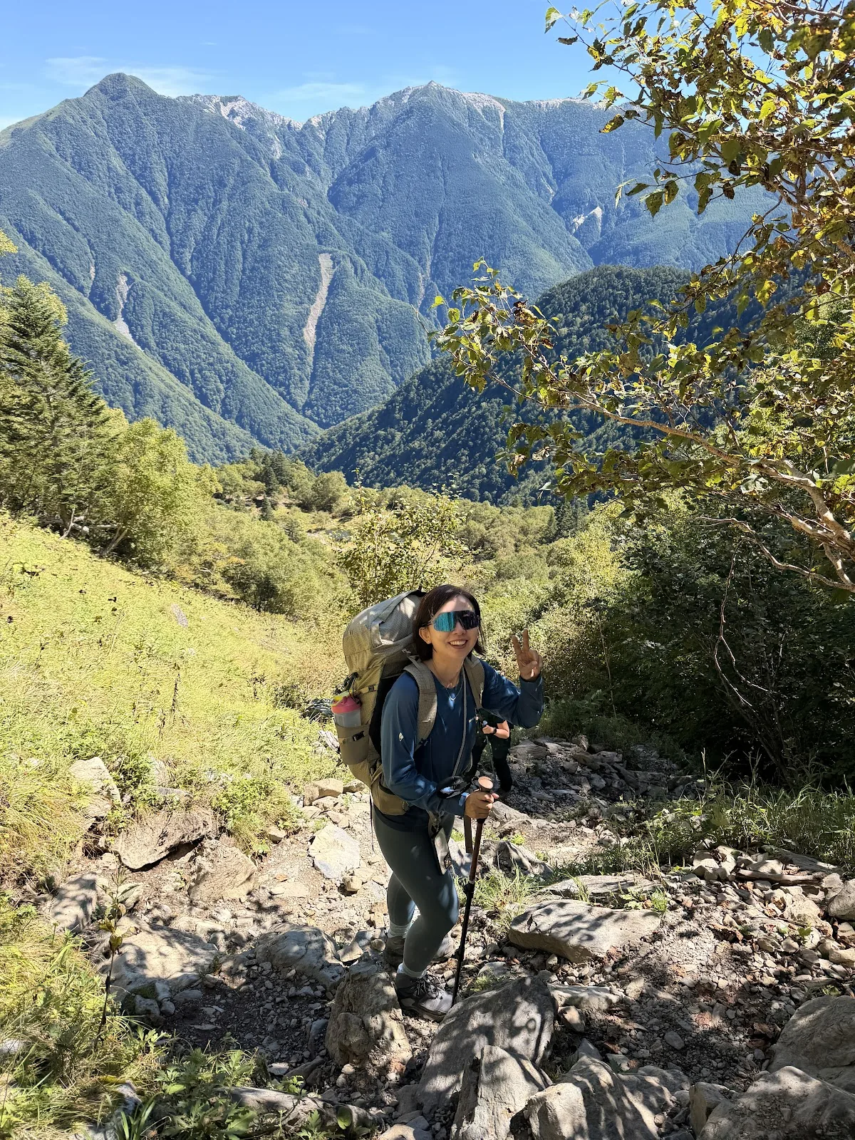 Hiker on a rocky trail below a huge mountain ridge